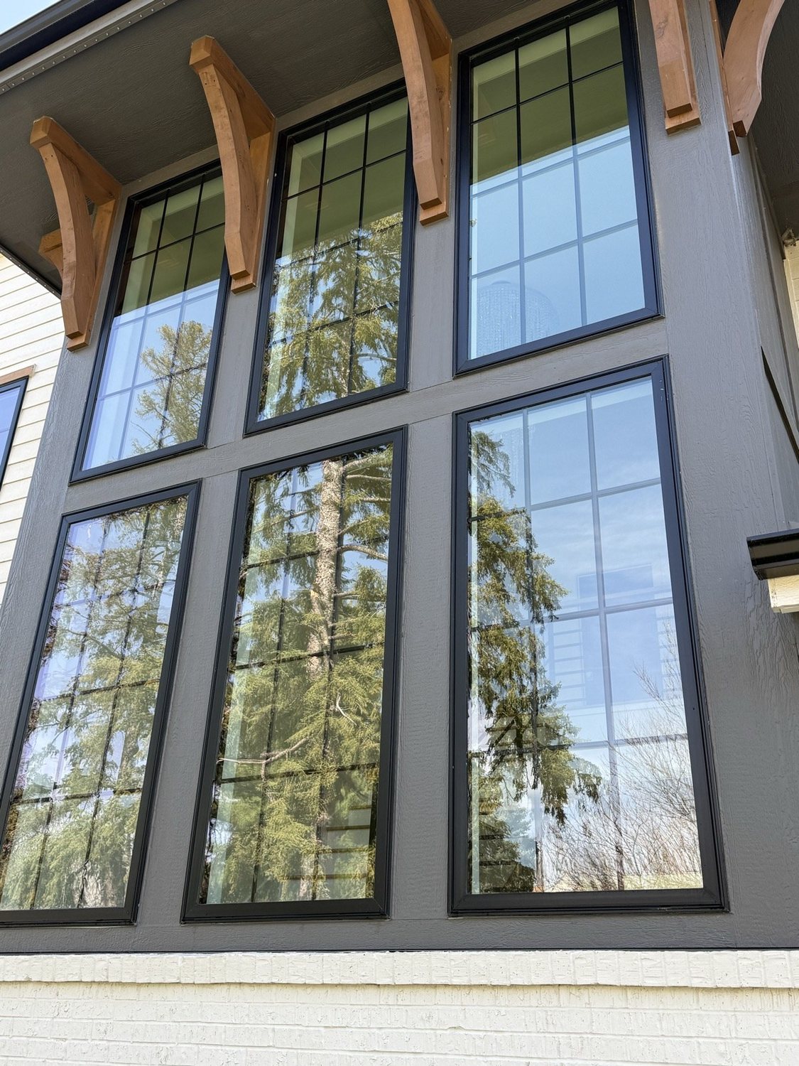 Spotless black-framed windows on a Sioux Falls home reflecting tall pine trees